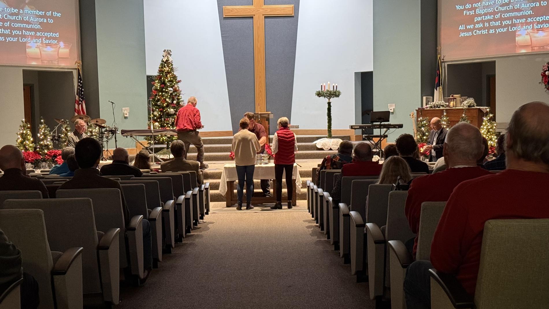 Church interior with people sitting, large cross, and Christmas decorations.