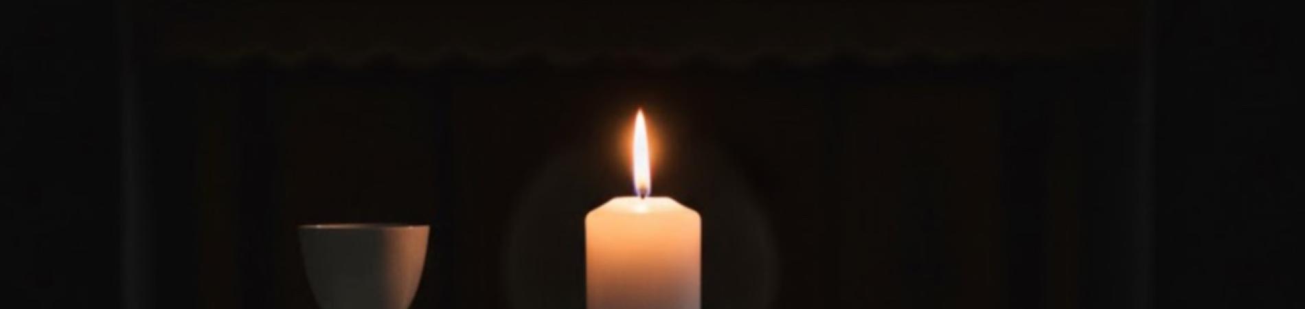 Candle, chalice, and bread on a table in a dimly lit setting.
