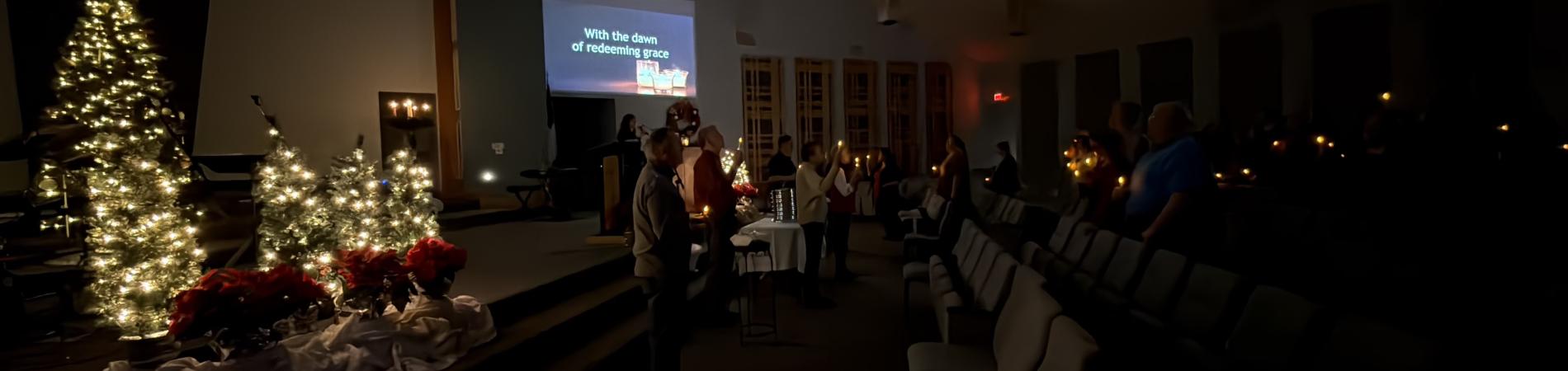 Dimly lit church interior with Christmas trees and a small group gathered.