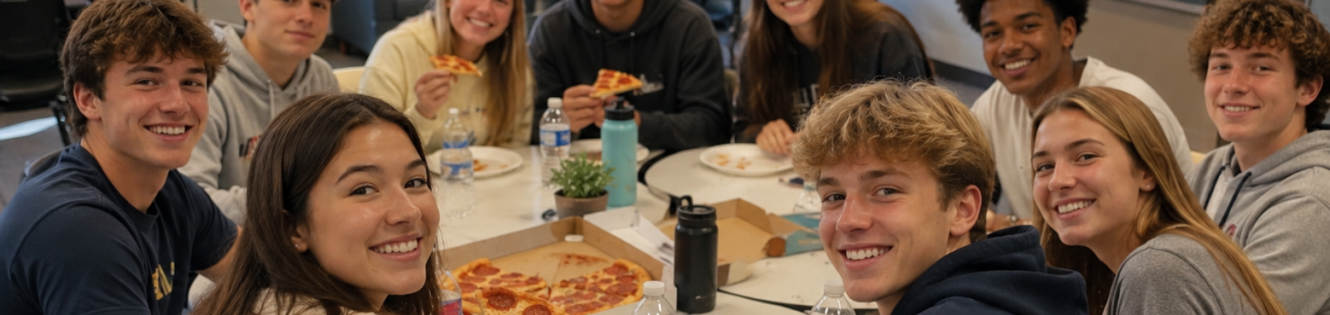 Group of young people smiling, sharing pizza around a table indoors.