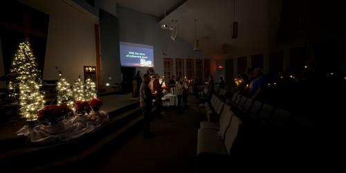 Dimly lit church interior with Christmas trees and a small group gathered.